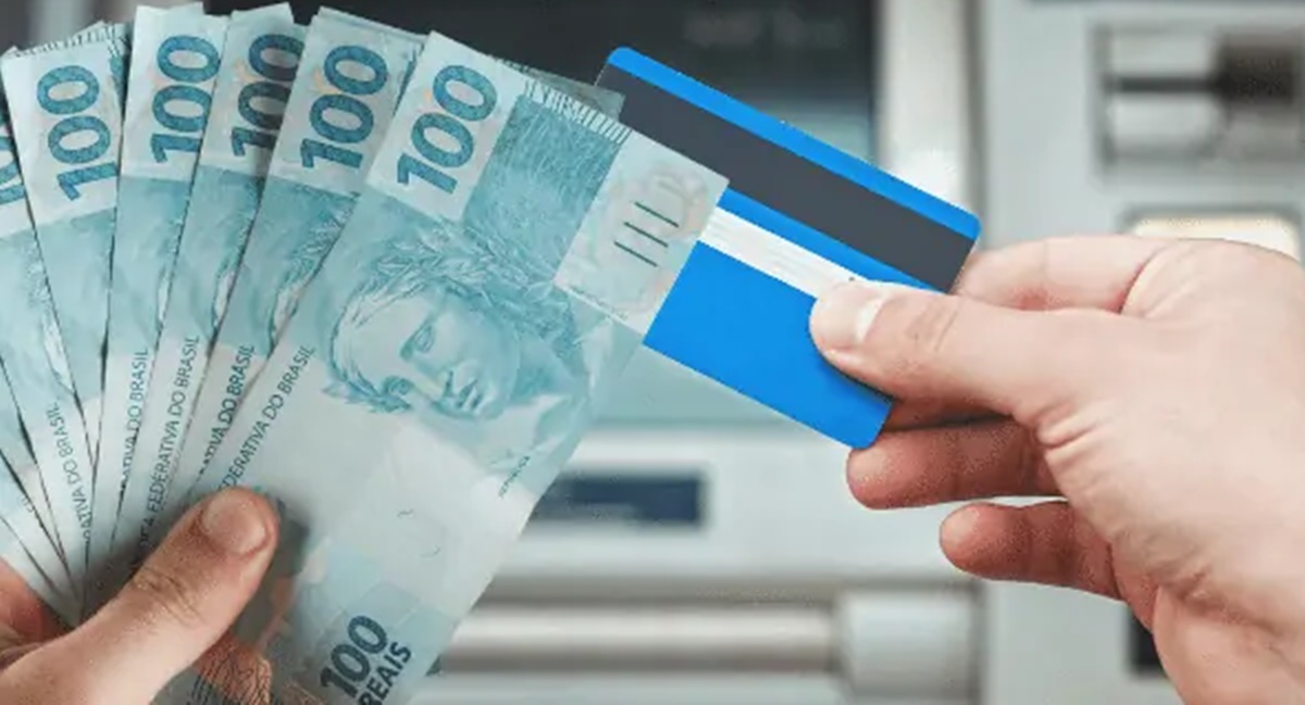 Trabalhador com seu cartão em caixa eletrônico após ter feito saque (Foto: Reprodução/ Internet)